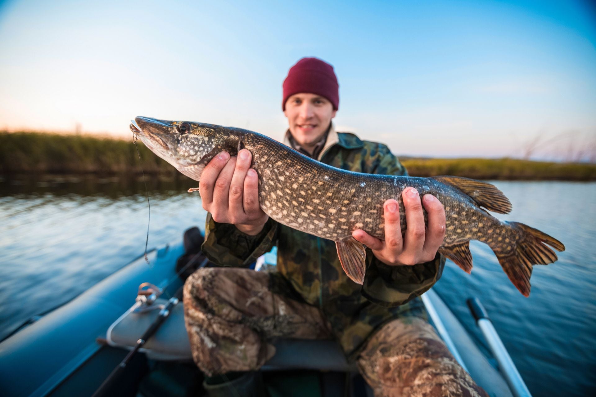Man holding a large fish on a boat with a lake and sky background